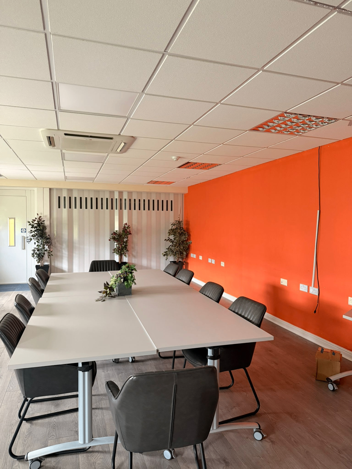 Upstairs conference room with flexible table layout, black chairs and an orange feature wall