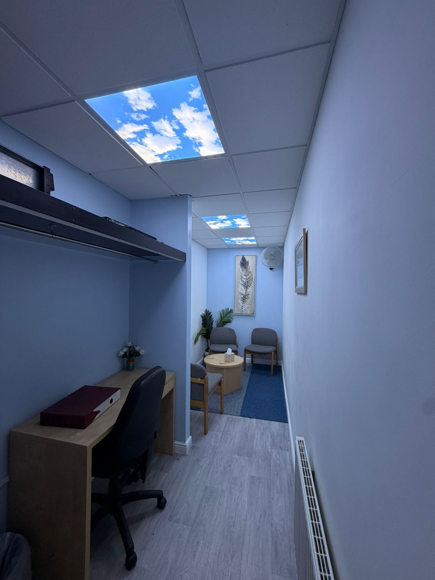 Breakout room with a blue-sky ceiling panel, soft chairs and a small round table