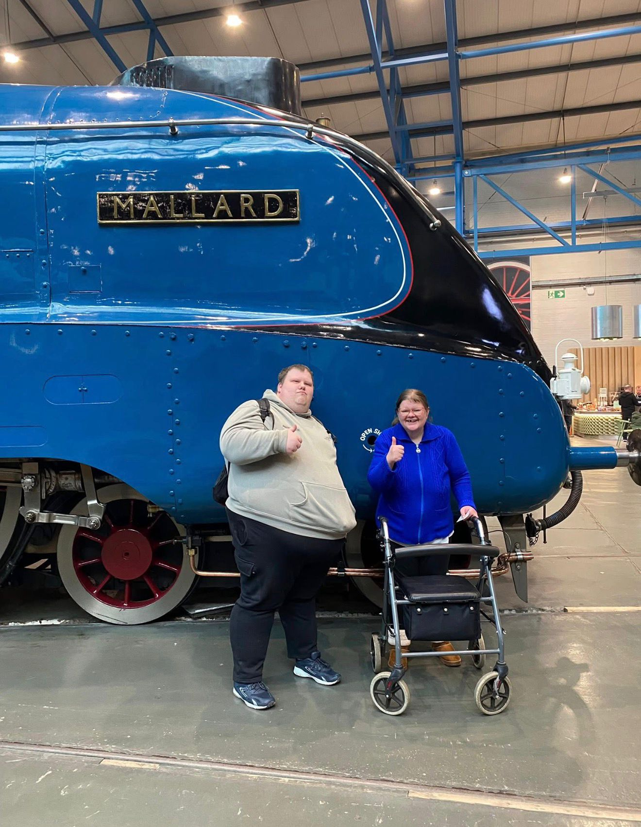 Two friends giving a thumbs up in front of the Mallard locomotive on a communitea day out