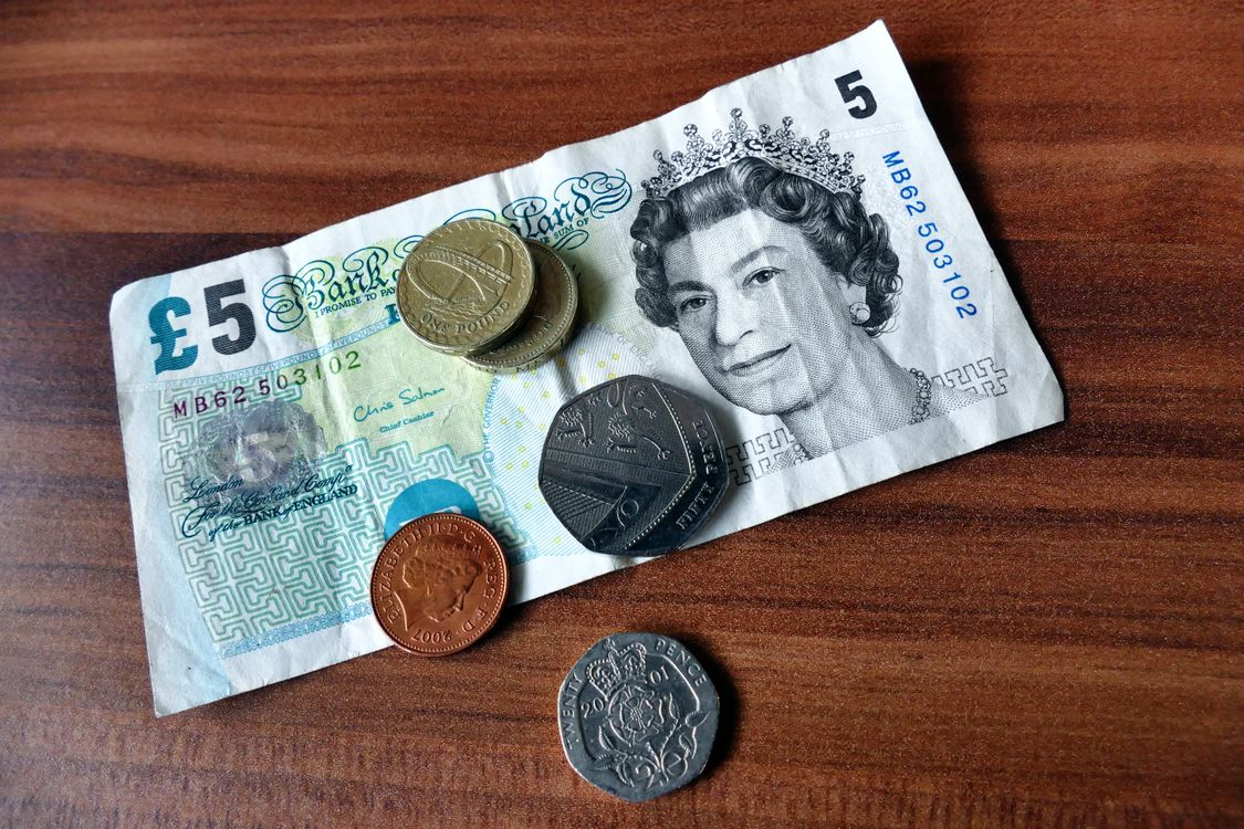 A five pound note with coins on a wooden table