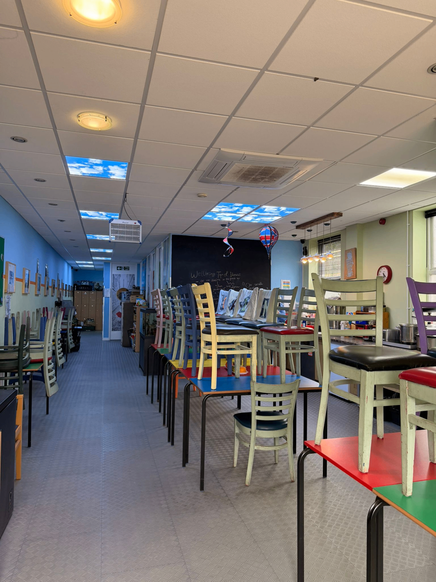 Long open social area with rows of tables, colourful chairs and sky-panel ceiling lights